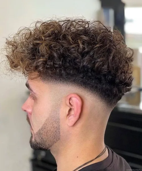 Low skin fade haircut with sharp sides and textured curls on top for a clean, modern look