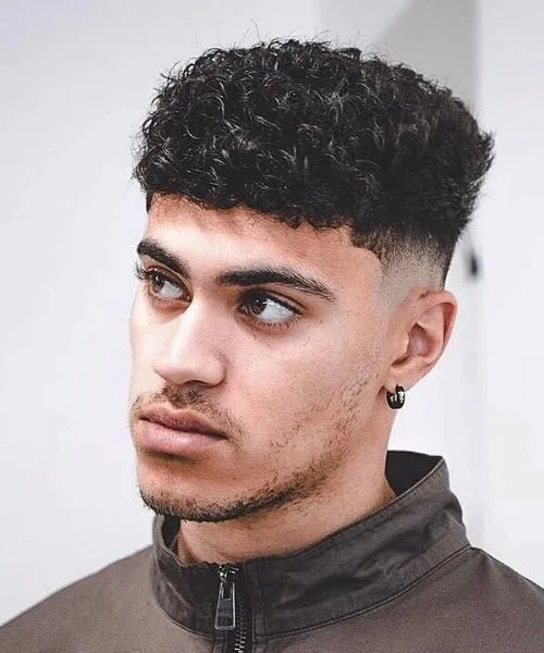 Curly Caesar haircut with tight faded sides, short straight fringe, and voluminous curls on top